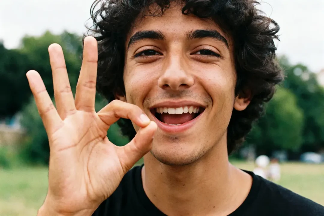 Jeune homme souriant faisant un signe de la main « OK » dans un parc verdoyant.