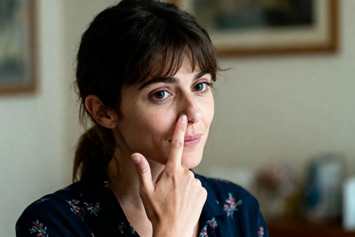 Femme portant une chemise à motifs floraux, touchant son nez avec son doigt, expression pensive.