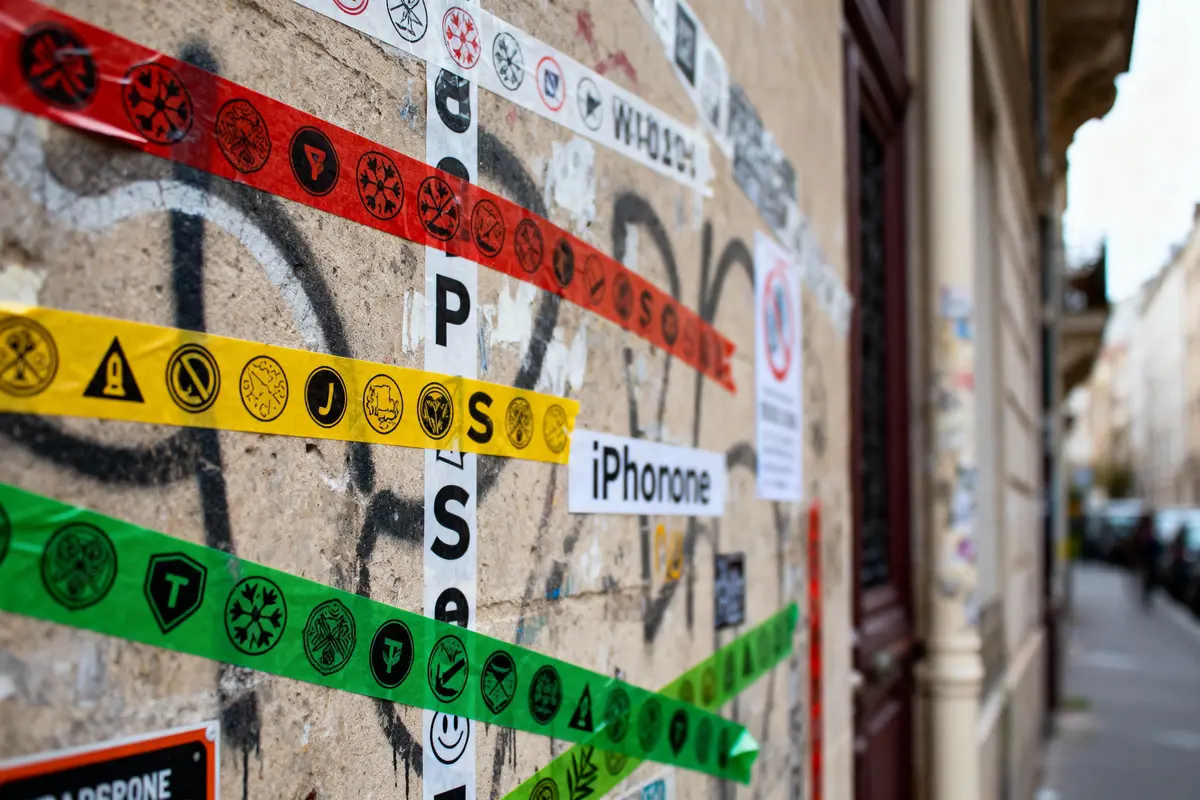 Mur couvert de bandes colorées et affiches avec des symboles variés sur fond de graffitis. Rue floue en arrière-plan.