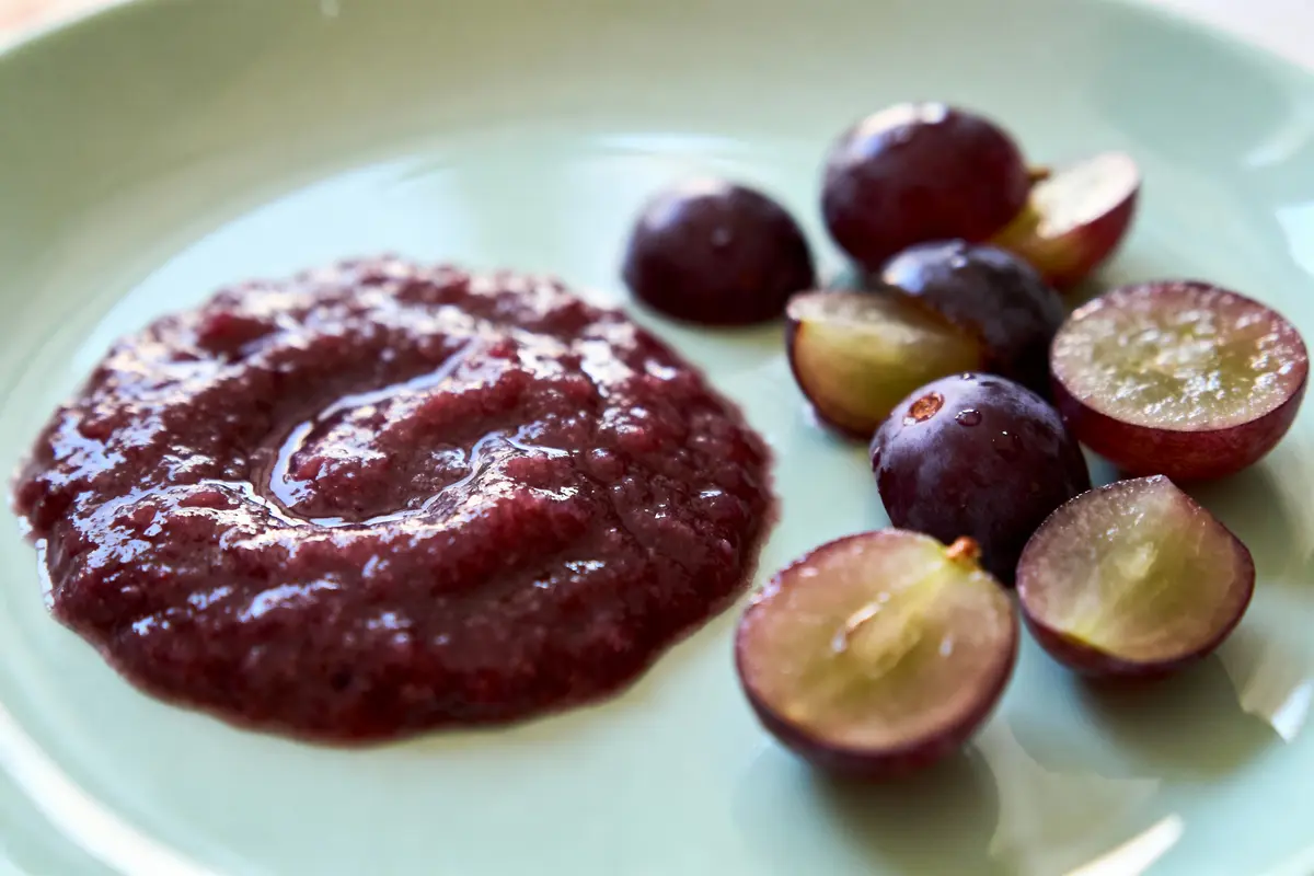 Compote de raisins rouges et raisins coupés en deux sur assiette verte.