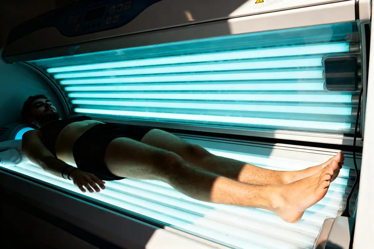 Personne allongée sur un lit de bronzage dans un solarium, lumière bleue des tubes fluorescents allumés.