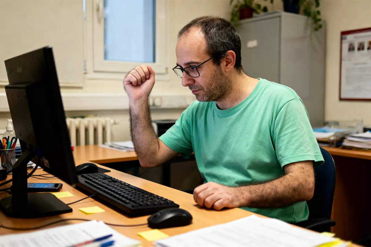 Homme concentré travaillant sur un ordinateur dans un bureau, vêtu d'un t-shirt vert.