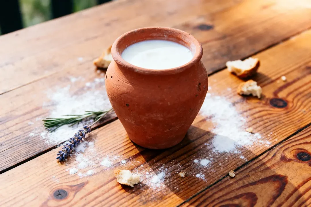 Pot en terre cuite avec lait sur table en bois, brin de lavande, miettes de pain, farine dispersée.