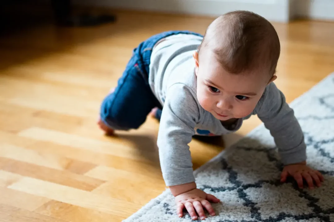 Bébé rampe sur le sol en bois et tapis, concentré et curieux.