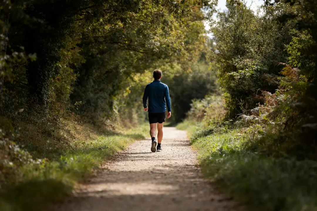 Homme marchant dans un chemin forestier ombragé mesurant sa vitesse moyenne de marche
