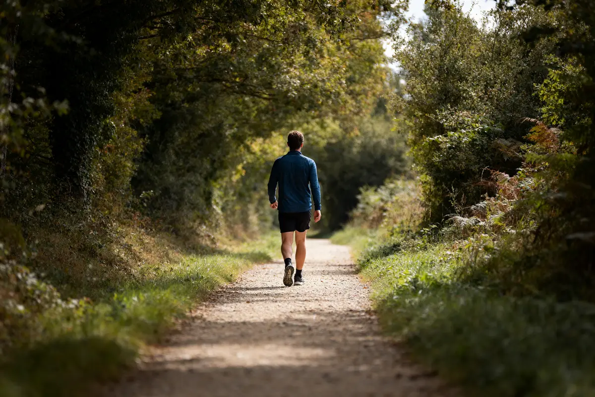 Homme marchant dans un chemin forestier ombragé mesurant sa vitesse moyenne de marche