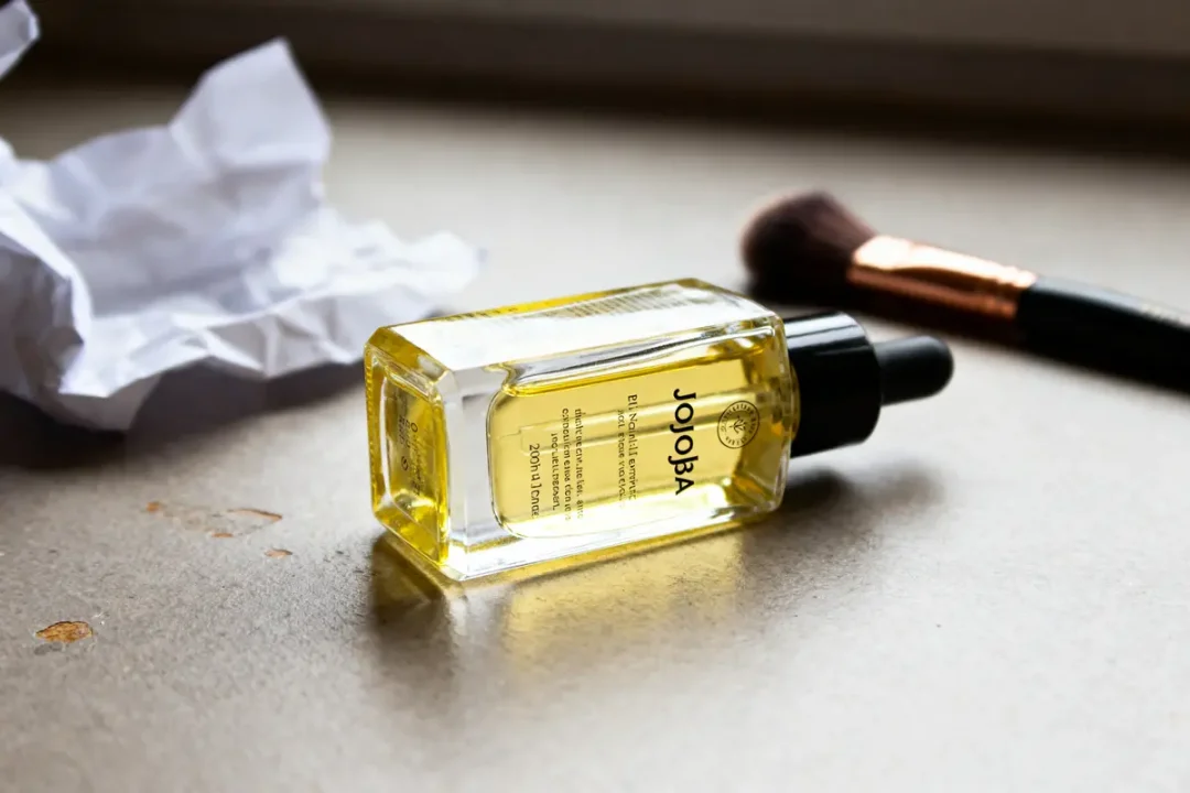 Bouteille d'huile de jojoba posée près d'un pinceau, recommandée par les dermatologues