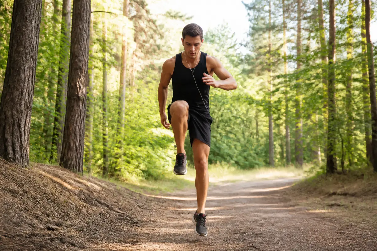 Un homme fait du jogging sur un sentier forestier, en tenue sportive noire.