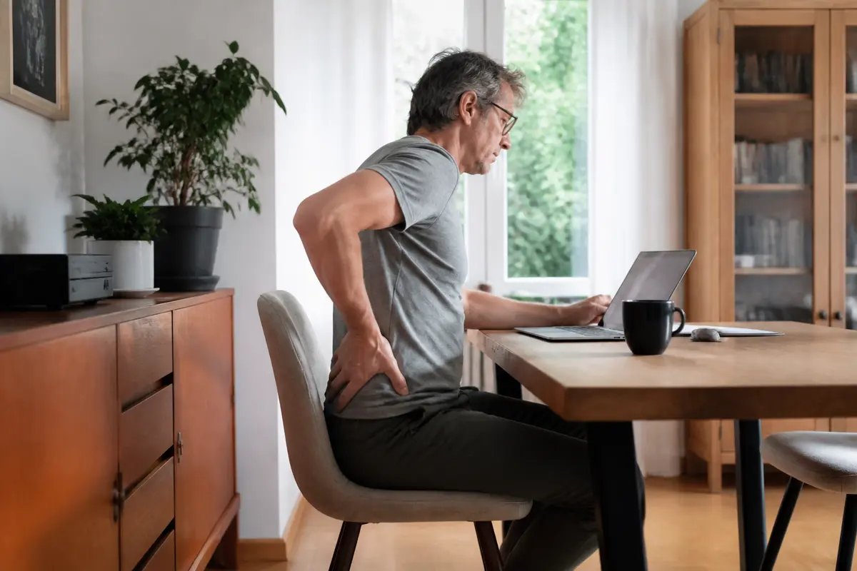 Un homme ressent une douleur au dos en travaillant à l'ordinateur dans un bureau à domicile.